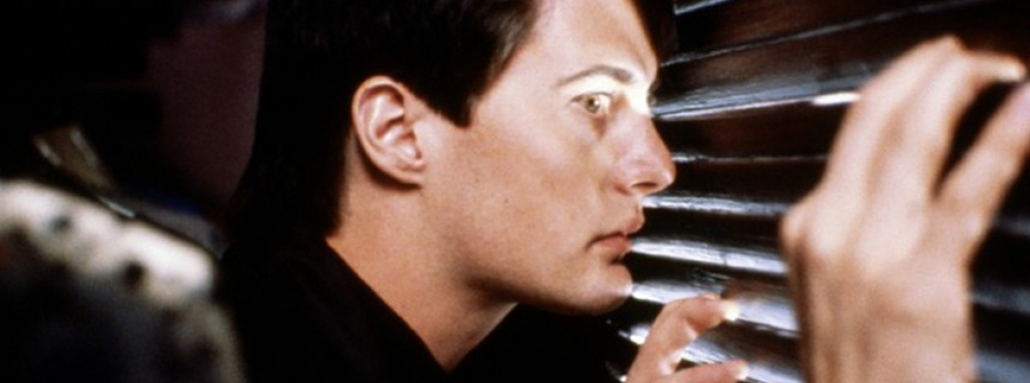 A dark-haired young man peers through the slats of a closet door, shocked by what he's seeing